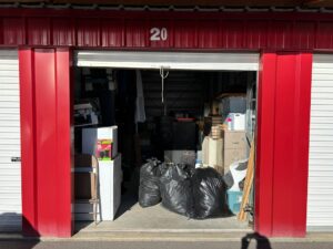 A person labels boxes beside neatly arranged furniture and seasonal household items in a clean storage space.
