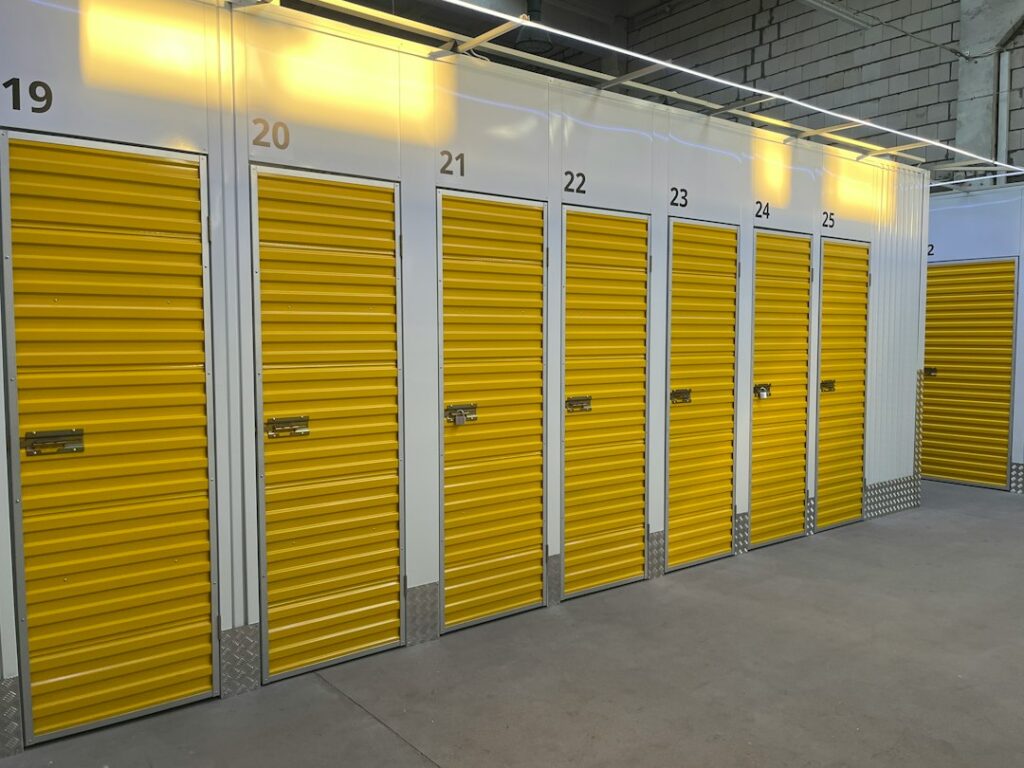 Person sweeping a tidy storage unit with labeled boxes elevated on shelving and furniture covered for protection.