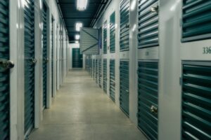 People load labeled boxes and covered furniture into a clean, organized storage unit.