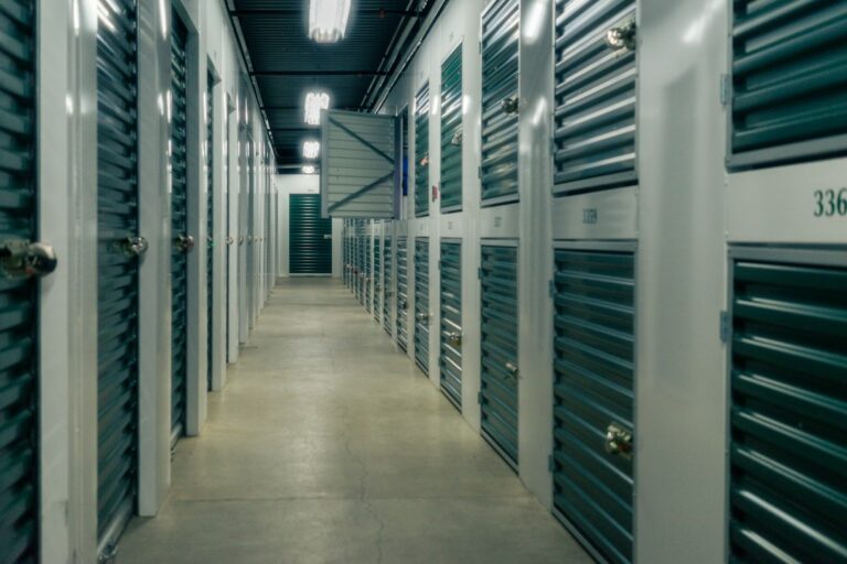 People load labeled boxes and covered furniture into a clean, organized storage unit.